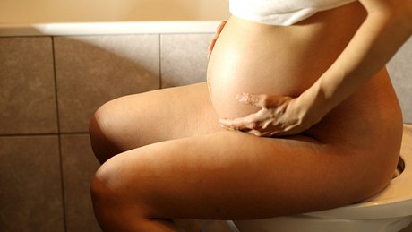 Schwangere Frau sitzt auf Toilette - Foto: iStock/lizalica