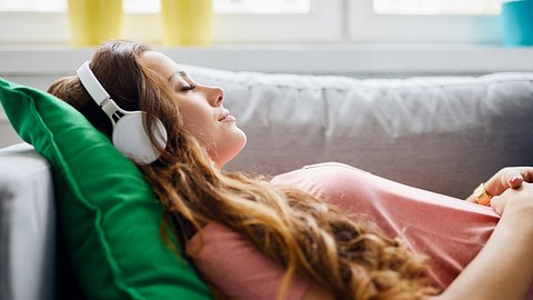 Junge Frau liegt auf dem Sofa und hört Musik - Foto: iStock/BartekSzewczyk