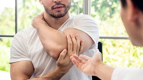 Mann hält seinen schmerzenden Arm fest - Foto: istock/kritchanut