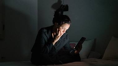 Frau im Dunklen schaut aufs Handy - Foto: iStock/Orbon Alija