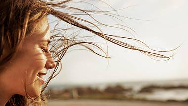 Frau steht im Wind und lächelt - Foto: istock/pixdeluxe