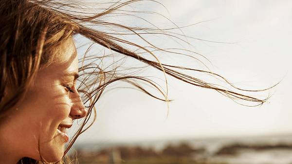 Frau steht im Wind und lächelt - Foto: istock/pixdeluxe