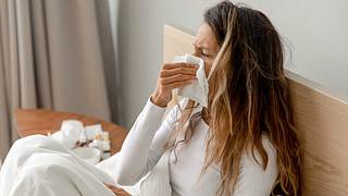 Frau im Bett putzt sich die Nase - Foto: iStock/ fizkes