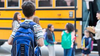Kleiner Junge steht vor dem Schulbus und schaut ihn an - Foto: istock_SDIProductions