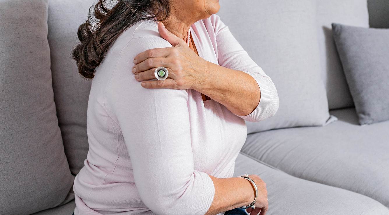schultergelenk-schmerzen Frau auf dem Sofa hält sich die linke Schulter
