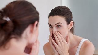 Frau kontrolliert ihr Gesicht in einem Spiegel - Foto: iStock/jeffbergen