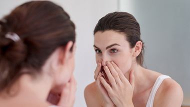Frau kontrolliert ihr Gesicht in einem Spiegel - Foto: iStock/jeffbergen