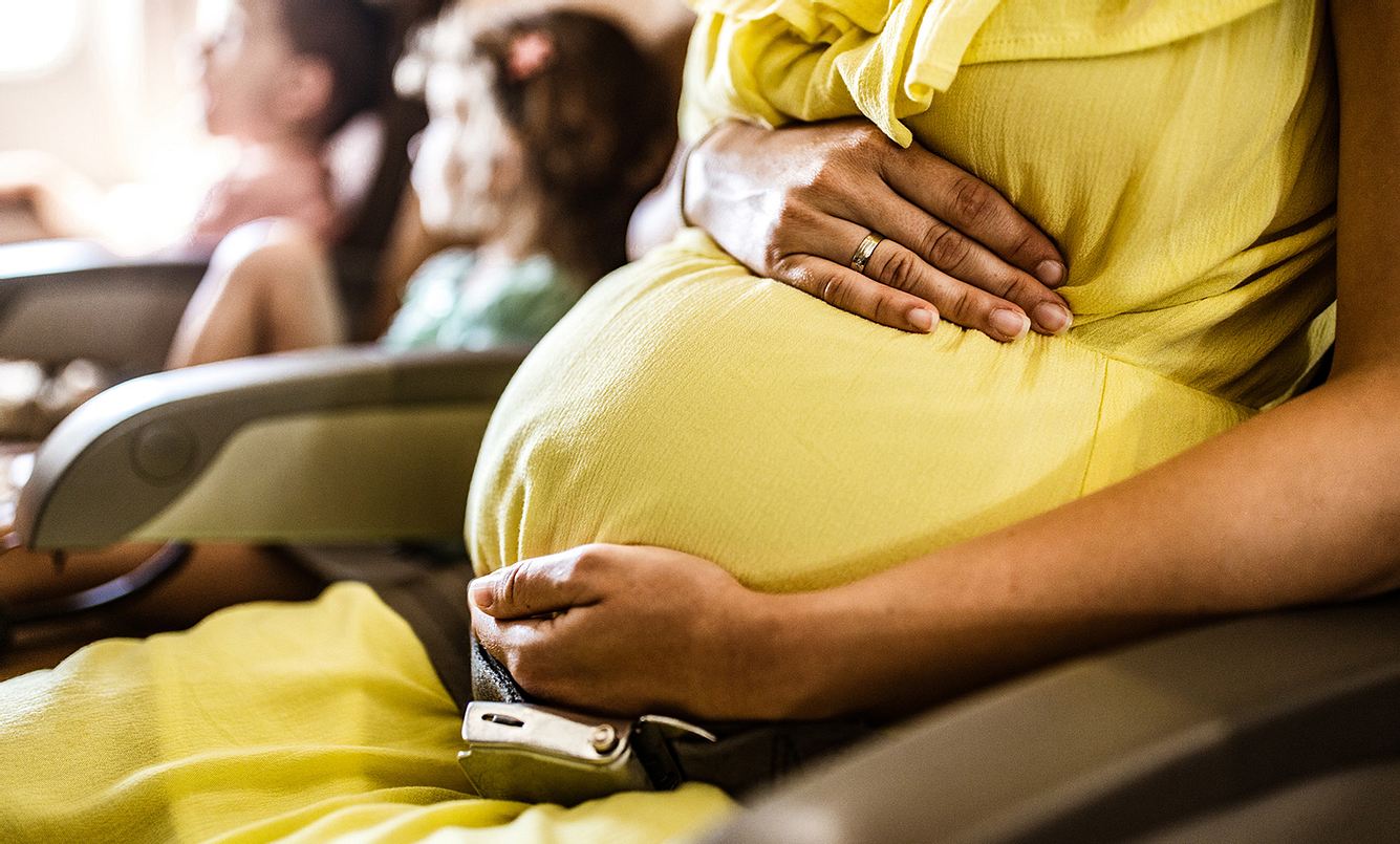 Schwangere Frau sitzt im Flugzeug und hält sich den Bauch.