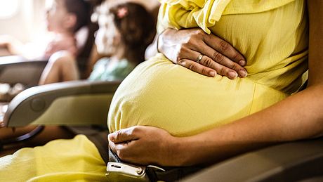 Schwangere Frau sitzt im Flugzeug und hält sich den Bauch. - Foto: iStock / skynesher