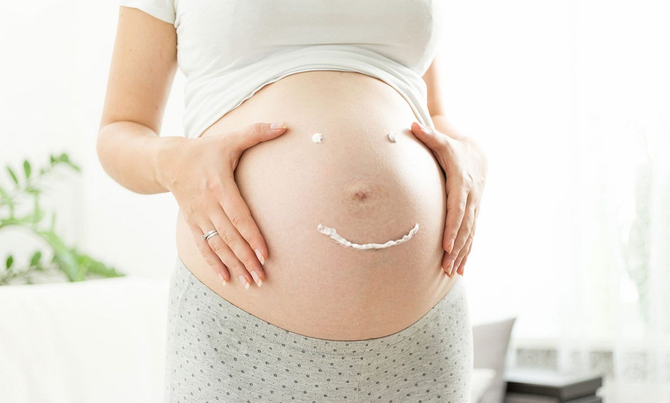 Schwangere Frau malt Smiley mit Creme auf ihren Bauch