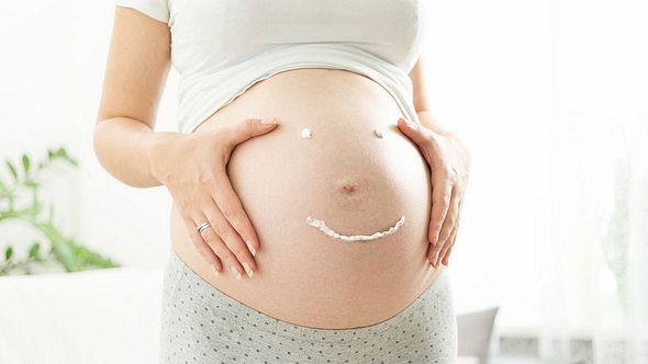 Schwangere Frau malt Smiley mit Creme auf ihren Bauch - Foto: iStock/Artfoliophoto