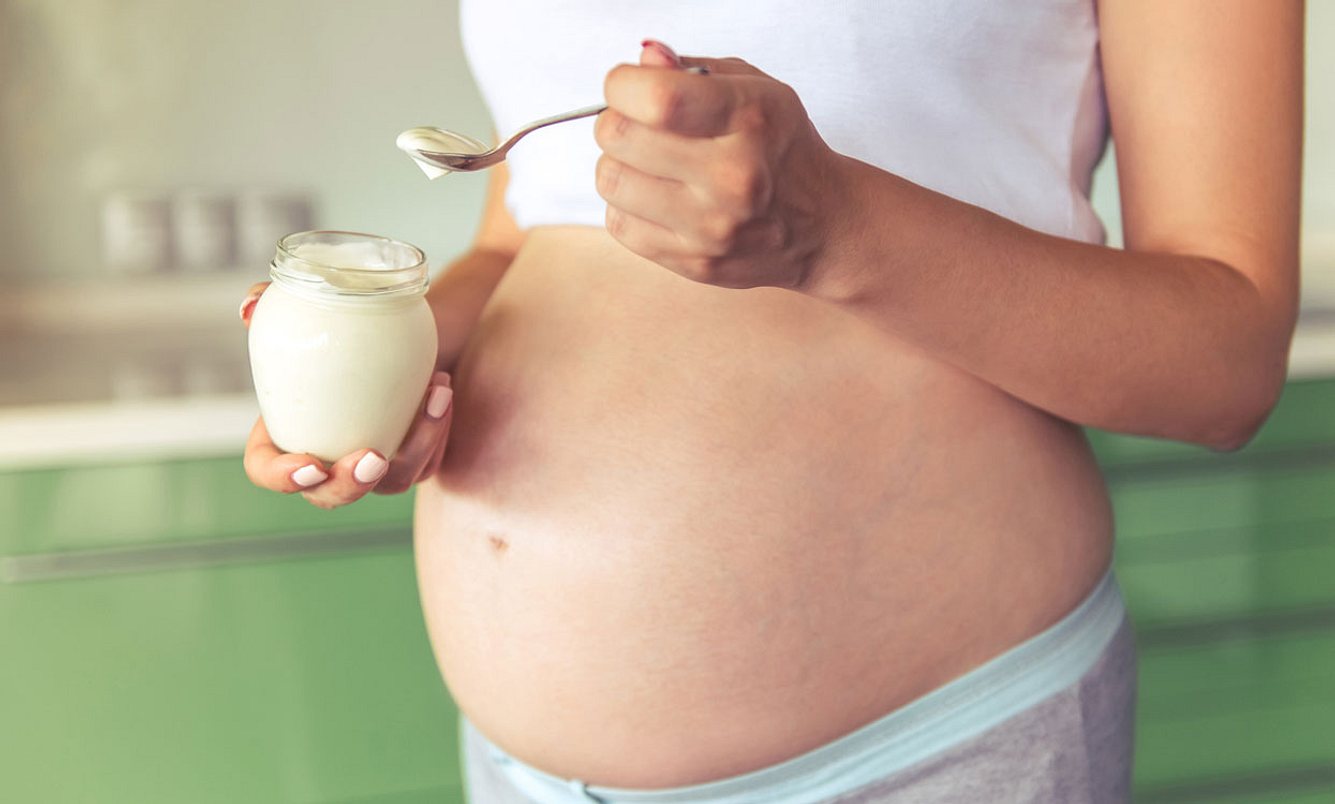 Schwangere Frau steht in der Küche und isst Joghurt