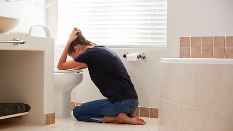 Eine Frau kniet mit abgestützten Armen vor einer Toilette, um sich zu übergeben - Foto: istock_monkeybusinessimages