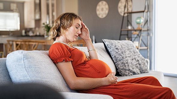 Eine schwangere Frau sitzt erschöpft auf dem Sofa - Foto: iStock_Ridofranz