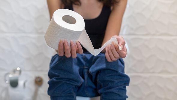 Frau sitzt auf der Toilette und hält eine Rolle Toilettenpapier in der Hand - Foto: iStock / bymuratdeniz