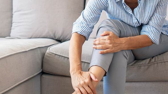 Oberkörper und beine einer Frau, die auf dem Sofa sitzt und ihre Hände an Knöchel und Knie legt - Foto: istock/﻿dragana991