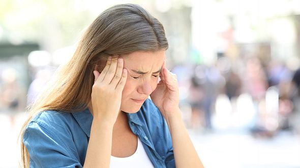 Junge Frau mit Schwindel und Kopfschmerzen fasst sich an den Kopf - Foto: iStock/AntonioGuillem