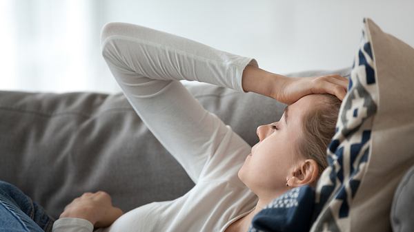 Eine Frau liegt mit Schwindel auf dem Sofa und fasst sich an den Kopf - Foto: iStock_fizkes