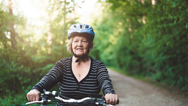 Eine ältere Frau fährt mit dem Fahrrad durch ein Waldstück - Foto: iStock_Ziga Plahutar