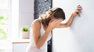 Frau im Top fasst sich an den Kopf und stützt sich an der Wand ab - Foto: iStock/AndreyPopov