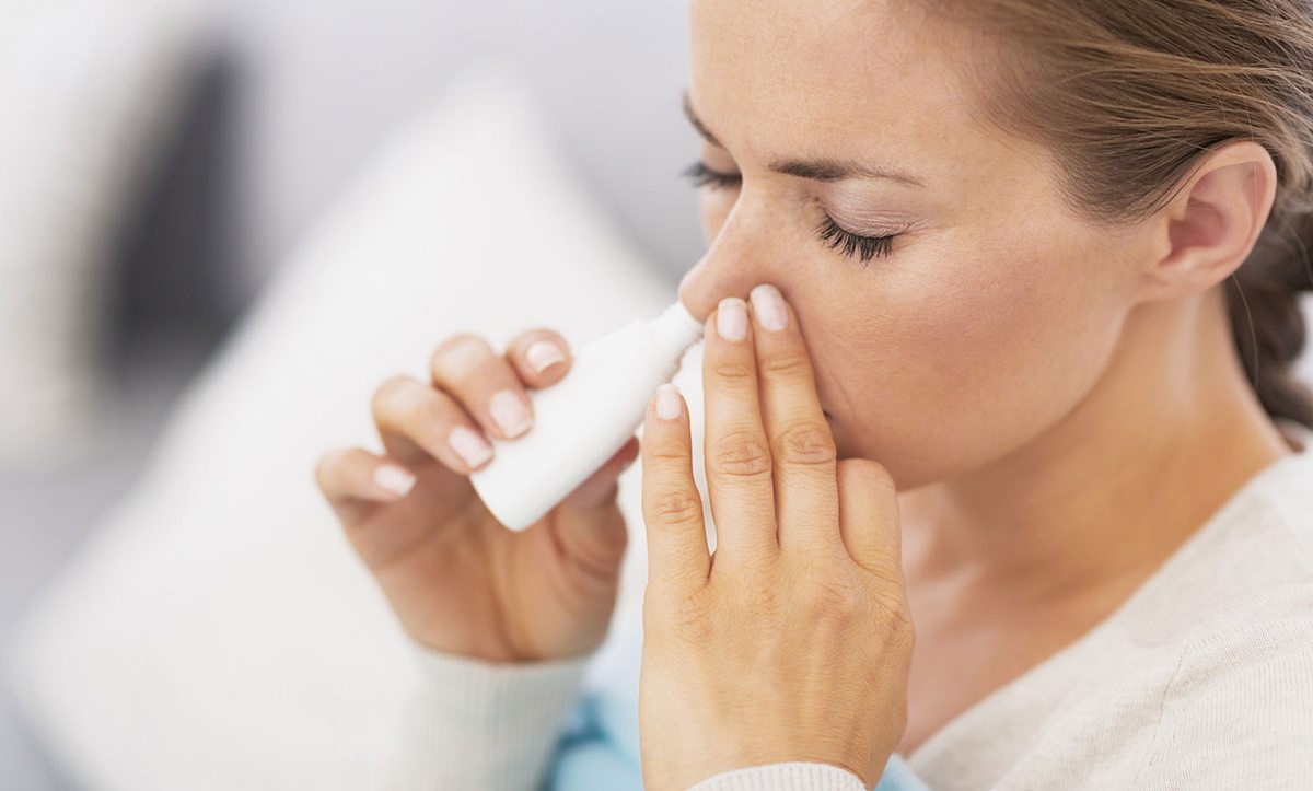 Eine Frau sprüht sich Nasenspray in die Nase