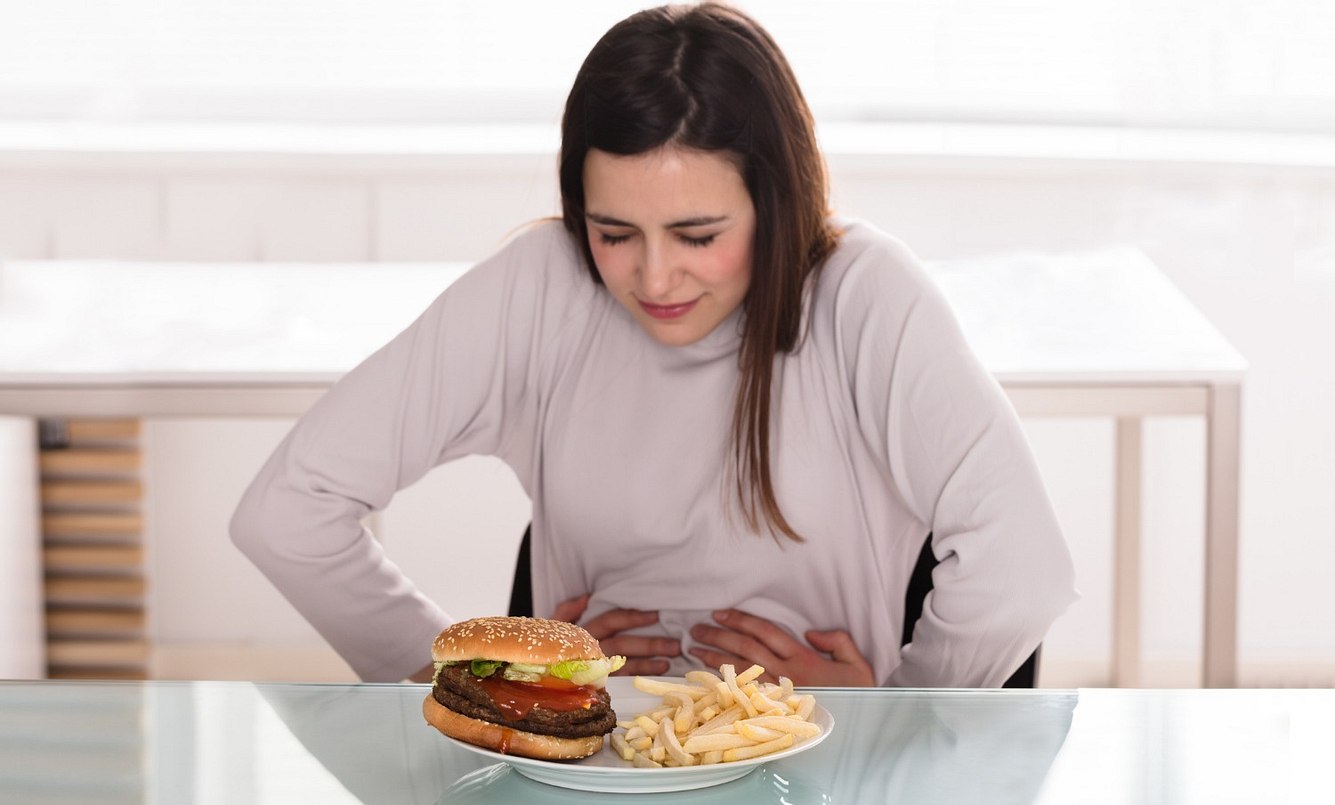Frau hält sich den Bauch und sitzt vor Burger und Pommes