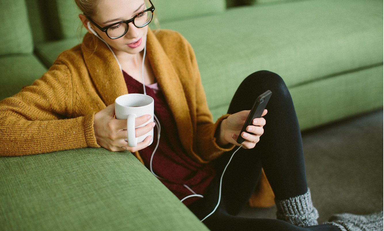 Eine Frau sitzt zu Hause auf dem Boden und hört Musik mit ihrem Smartphone