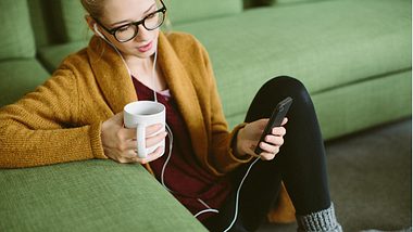 Eine Frau sitzt zu Hause auf dem Boden und hört Musik mit ihrem Smartphone - Foto: iStock/alvarez
