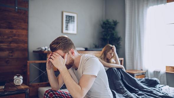 Paar im Bett, er sitzt am Bettrand und dreht ihr den Rücken zu, beide stützen den Kopf in die Hände - Foto: iStock/South_agency
