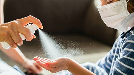 Mutter sprüht kleinem Mädchen mit Maske Desinfektionsmittel auf die Hand - Foto: iStock/skynesher