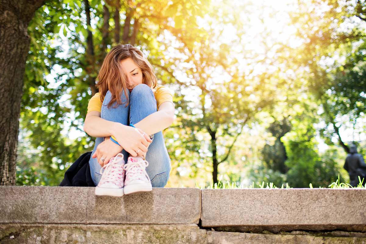 Junge Frau sitzt mit angezogenen Beinen auf einer Mauer