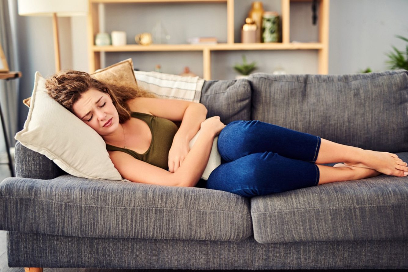 Sorbitintoleranz: Junge Frau liegt mit Bauchschmerzen auf dem Sofa