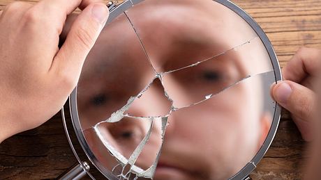 Mann blickt in einen zerbrochenen Spiegel - Foto: iStock/AndreyPopov