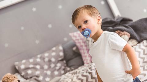 Junge mit Schnuller steht vor Bett - Foto: istock/georgerudy.