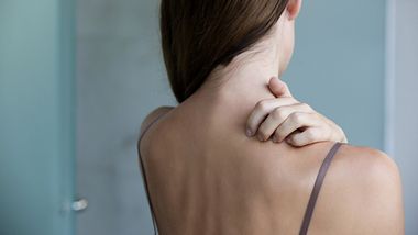 Eine Frau kratzt sich am Rücken - Foto: iStock/triocean
