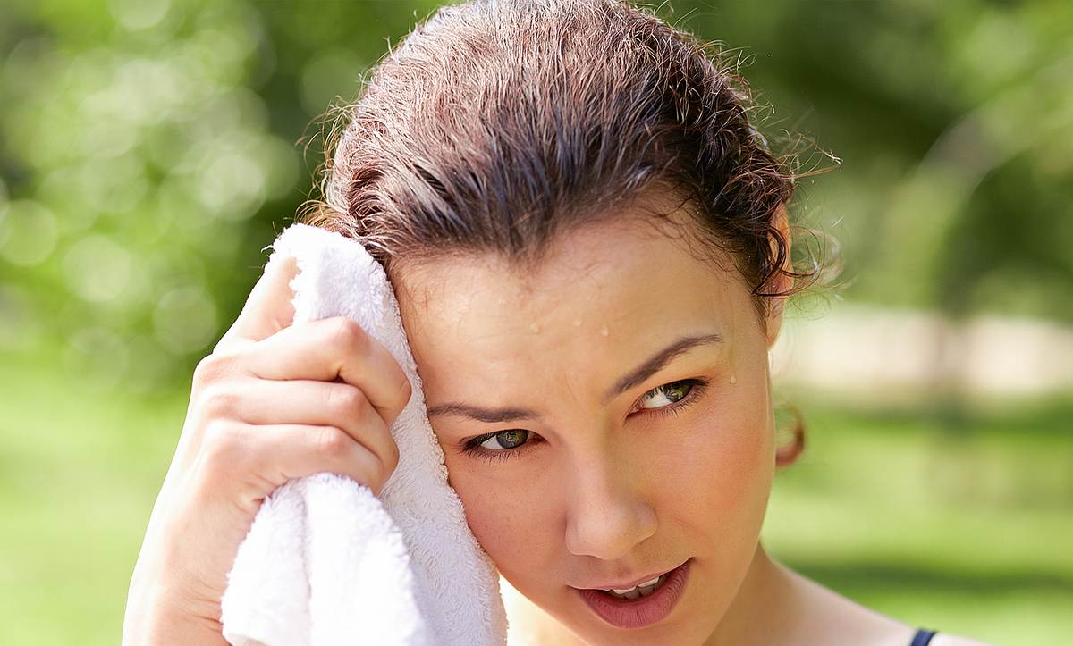 Frau wischt sich mit einem Handtuch den Schweiß von der Stirn.