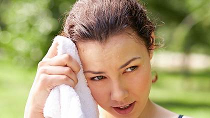 Frau wischt sich mit einem Handtuch den Schweiß von der Stirn. - Foto: IStock/mediaphotos