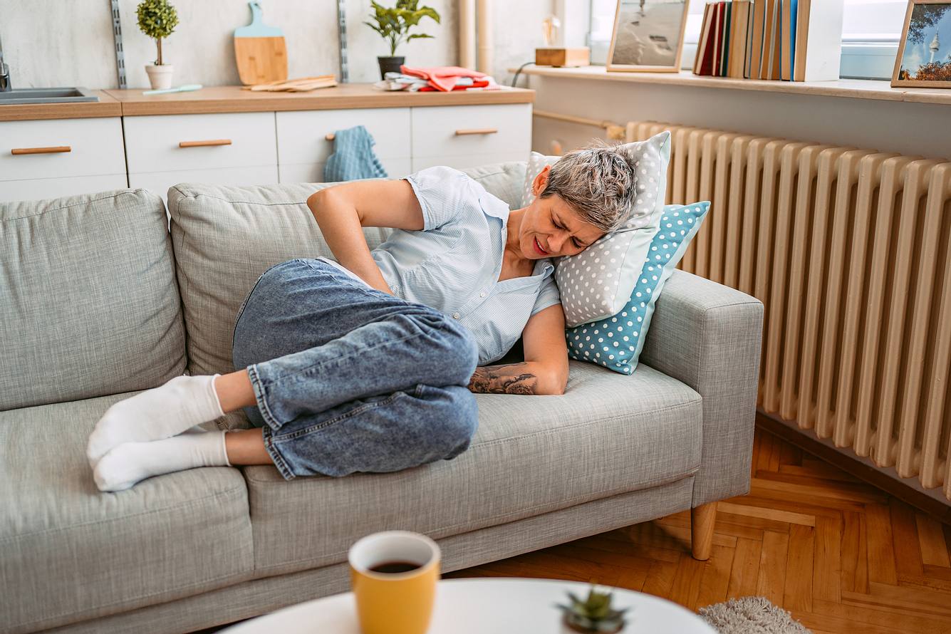 Frau mit starken Bauchschmerzen liegt auf dem Sofa 