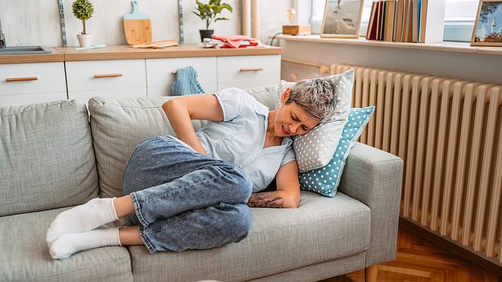 Frau mit starken Bauchschmerzen liegt auf dem Sofa  - Foto: iStock/urbazon
