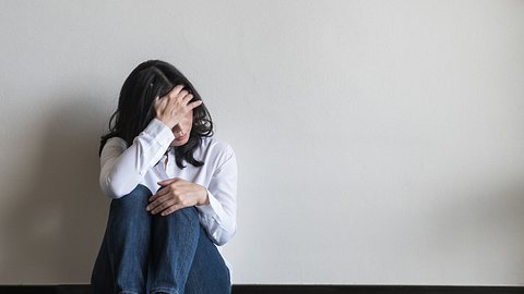 Eine erschöpfte Frau sitzt auf dem Boden und fasst sich an den Kopf - Foto: istock_hinnapong