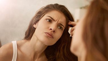 Junge Frau begutachten Stirnfalten vor dem Spiegel - Foto: iStock/bowie15