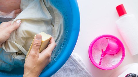 Person behandelt Stockflecken auf Kleidung mit Wasser und Schwamm - Foto: iStock/FotoDuets