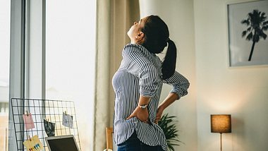 Eine Frau hält sich den schmerzenden Rücken - Foto: iStock_Charday Penn