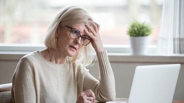 Ältere Frau am Schreibtisch fasst sich an den Kopf - Foto: iStock/fizkes