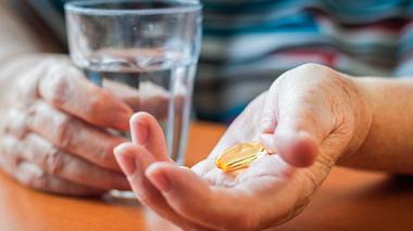 Tabletten und ein Wasserglas in der Hand - Foto: iStock / Zbynek Pospisil