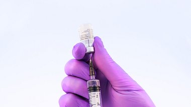 Hand mit lila Schutzhandschuh zieht Impfstoff aus Ampulle in Spritze auf - Foto: istock/﻿carmengabriela