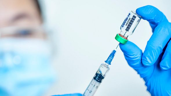 Corona-Impfstoff wird in Spritze aufgezogen, im Hintergrund Gesicht einer Ärztin mit Schutzmaske - Foto: iStock/Tomwang112 