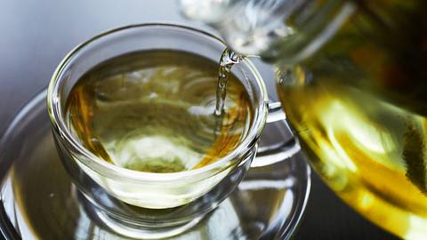 Tasse und Kanne, aus der grüner Tee eingeschenkt wird - Foto: iStock/millionsjoker