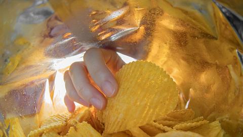 Hand, die in eine Tüte Chips greift - Foto: iStock/StockGood