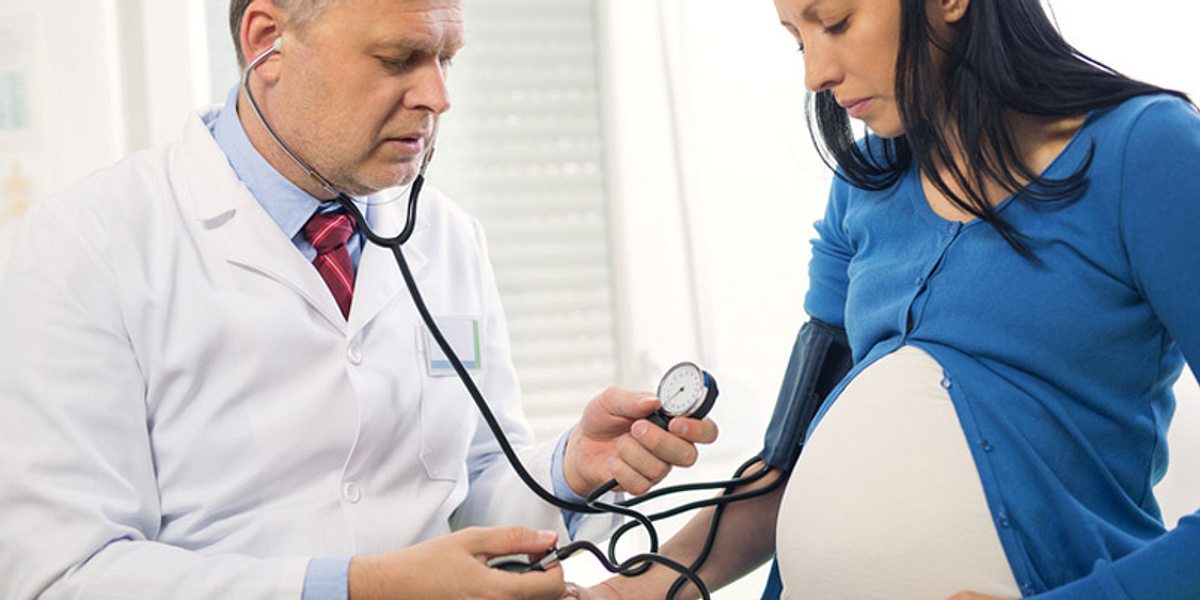 Ein Arzt kontrolliert bei einer schwangeren Frau den Blutdruck